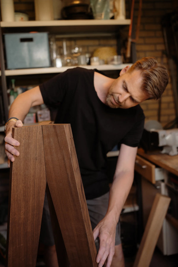 Alex houdt een houten onderstel vast in de werkplaats